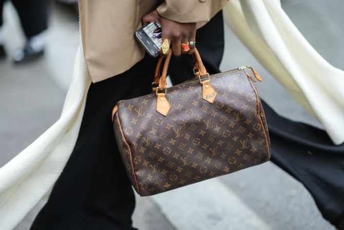 Vrouw met zwart Louis Vuitton tas met gouden logo en bruine jas